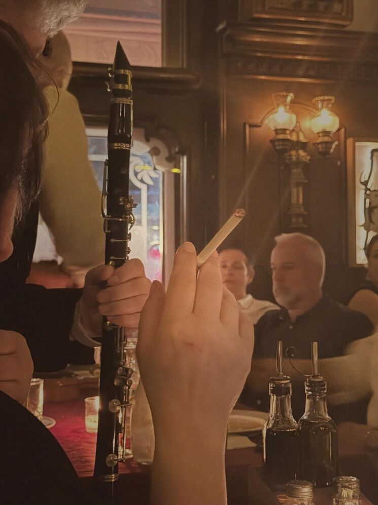 Person holding a black clarinet at a candlelit bar, with other patrons in the background.