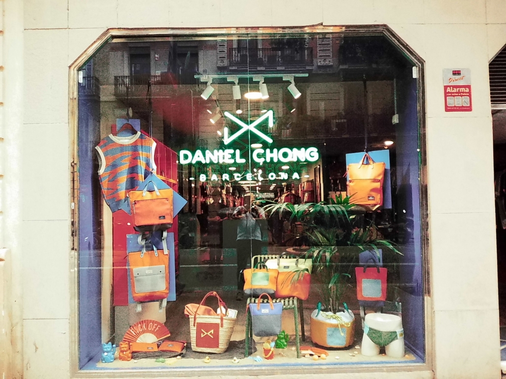 Block - Left - 5 of 16 - Petsolt Family Storefront window display for Daniel Chong with neon sign, colorful handbags, and clothing accessories arranged in mannequins and shelves.