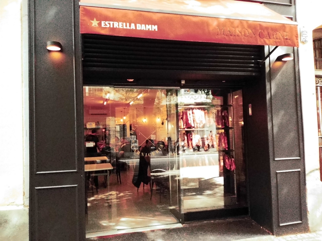 Block - Mountian - 10 of 13 - Petsolt Family Storefront with a glass display window showing clothing on racks and mannequins, under a red awning that reads Estrella Damm.
