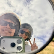 2026-02- Malta - 7 of 9 - Petsolt Family Person wearing helmet and sunglasses reflected in a round mirror, smiling at the camera outdoors, making a peace sign with fingers
