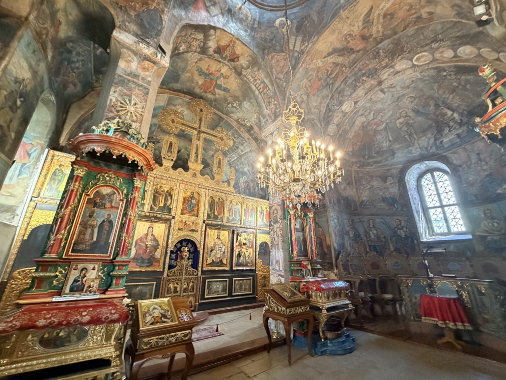 Ornate Orthodox church interior with gold iconostasis, icons, and a chandelier hanging above stone floor.