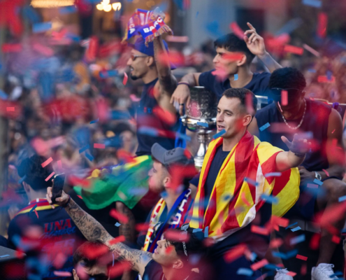 Crowd of celebrateers in Spain flag colors, confetti falling during a victory parade.