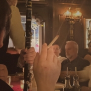 Person holding a black clarinet at a candlelit bar, with other patrons in the background.