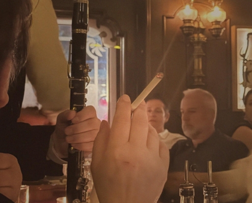 Person holding a black clarinet at a candlelit bar, with other patrons in the background.