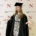Graduate in cap and gown gesturing with hands in front of a Northeastern University London backdrop.