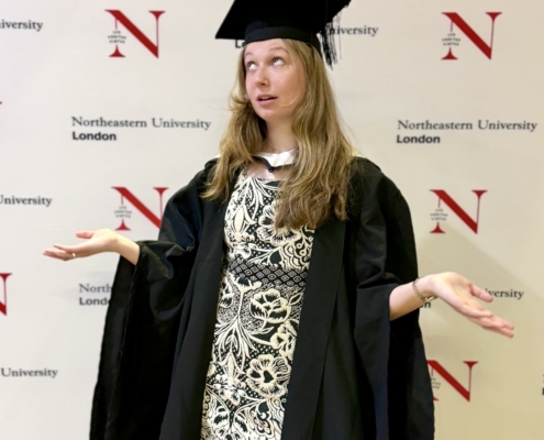 2026-07- London Ireland - 1 of 23 - Petsolt Family - Petsolt Family Graduate in cap and gown gesturing with hands in front of a Northeastern University London backdrop.