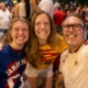 Three friends take a selfie in a crowded street crowd, all smiling and wearing colorful sports jerseys.