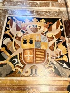 Decorative marble floor inlaid with a heraldic crest featuring a shield, crown, and floral motifs.