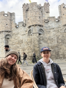 Casteling in Ghent Two friends smile for a photo in front of a medieval stone castle with towers behind them.