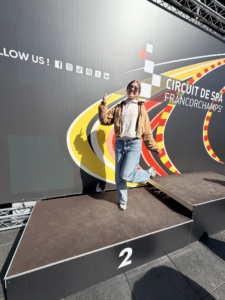 Setting expectations Woman posing on a second-place podium at Circuit de Spa-Francorchamps, smiling and making a rock-on gesture in sunglasses and casual clothing.