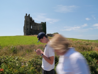 Ruined stone castle on a grassy hill under a blue sky, with several blurred visitors in the foreground.