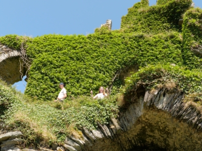Two people stand near a ivy-covered rocky cliff with a bright blue sky above.