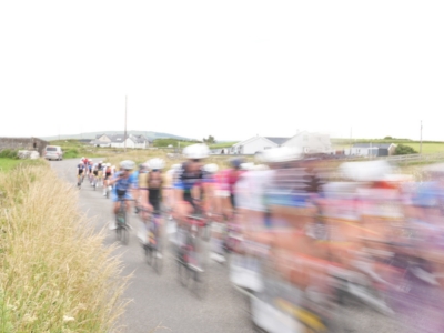 Cyclists racing along a rural road with houses in the background, motion blurred showing speed and movement