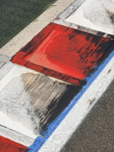 Diagonal curb with red, white, and blue paint on a rough asphalt surface, likely a street boundary marker or decorative curb edge.