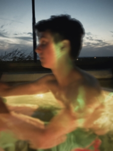 Blurry side-profile of a person outdoors at dusk with colorful lights on their face and shoulders.