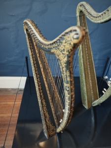 Close-up of an ornate antique harp with gold floral detailing against a blue wall.
